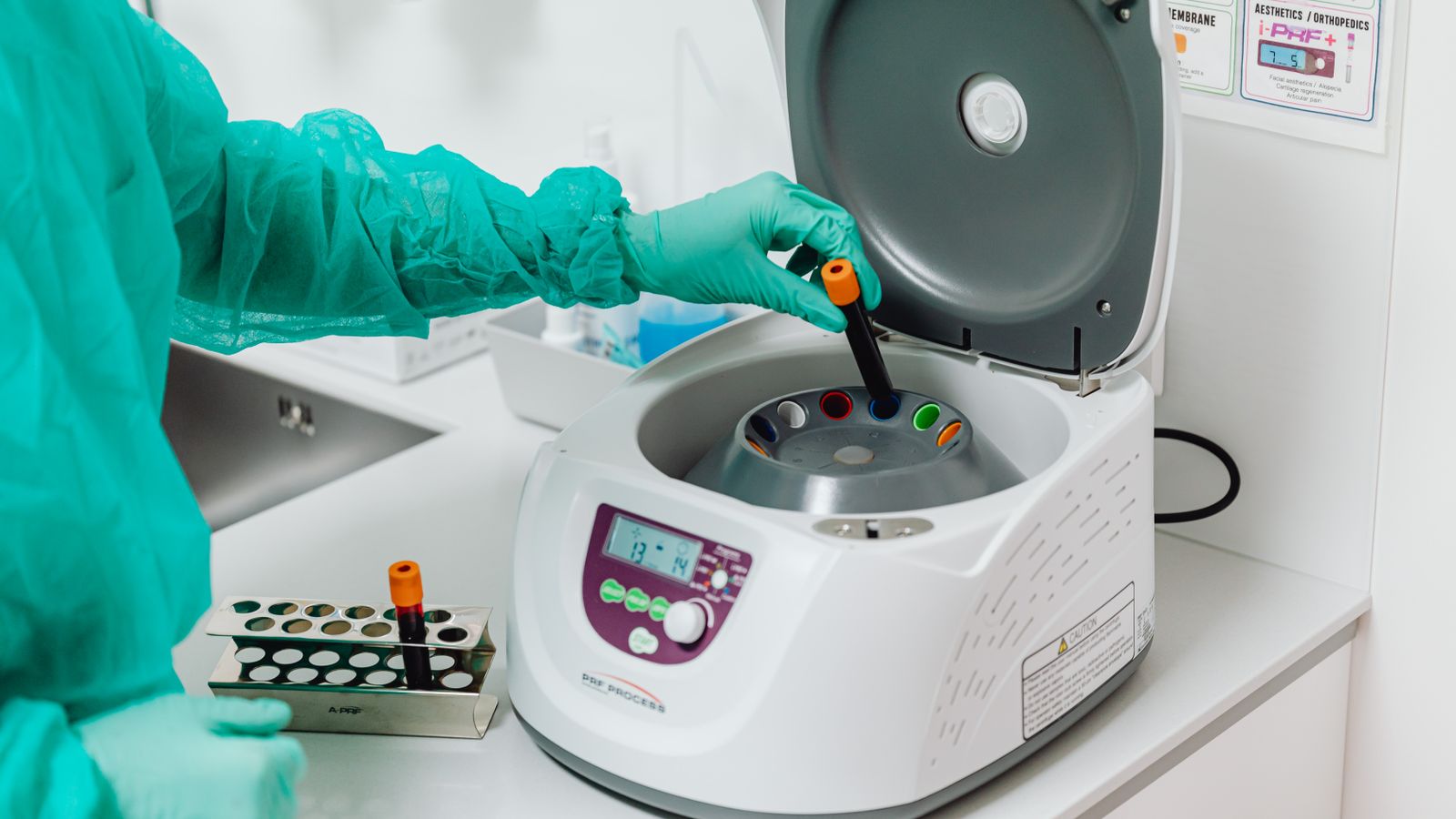 A healthcare professional in a lab coat operates a centrifuge in a sterile laboratory setting.