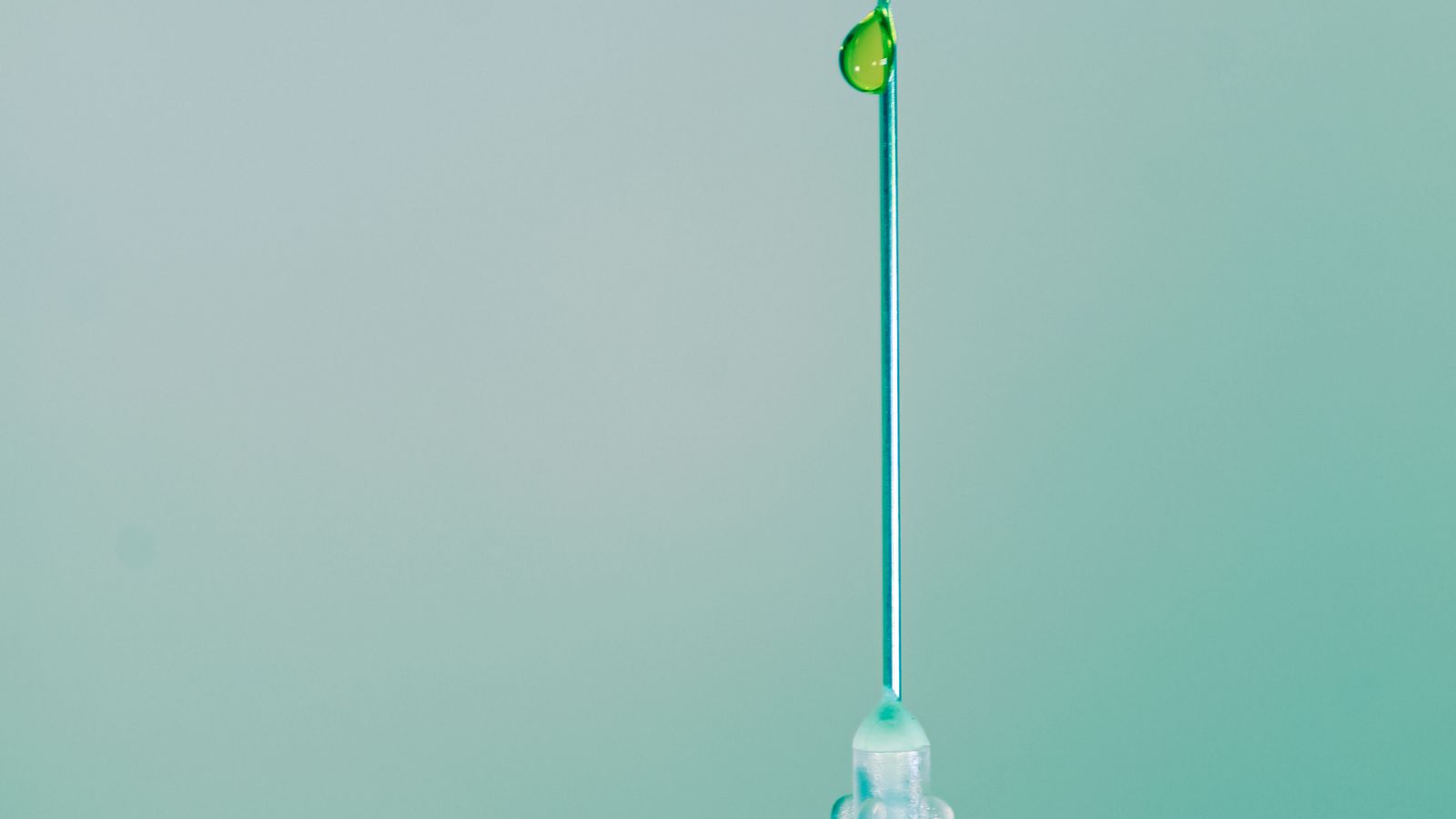 Close-up of a green-tinted syringe with a droplet of liquid at the needle tip